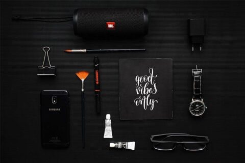 Mockup of various items like a speaker, charger brick, mini toothpaste, phone case & watch in a nice layout all items are black on a slightly lighter black background