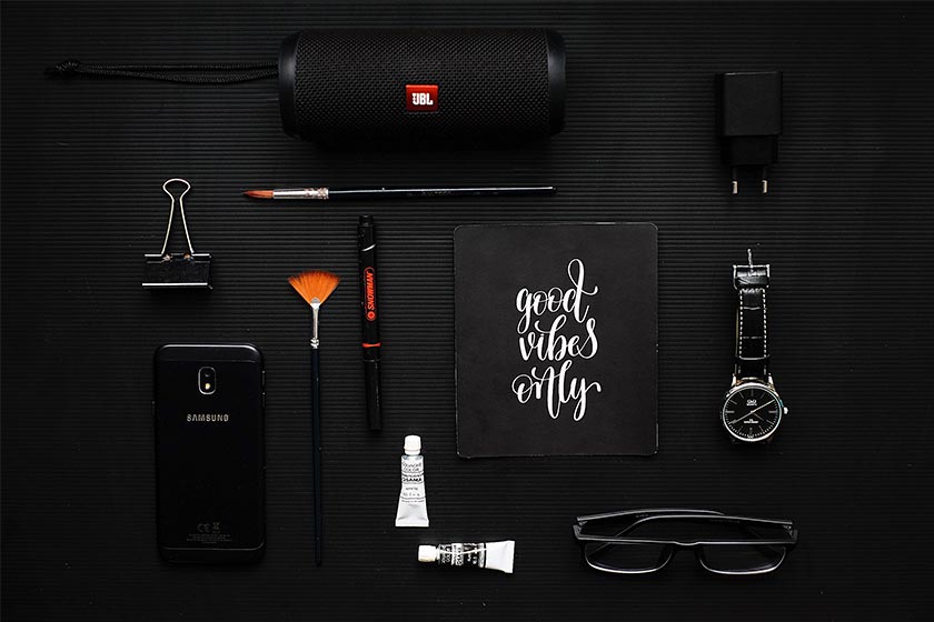 Mockup of various items like a speaker, charger brick, mini toothpaste, phone case & watch in a nice layout all items are black on a slightly lighter black background